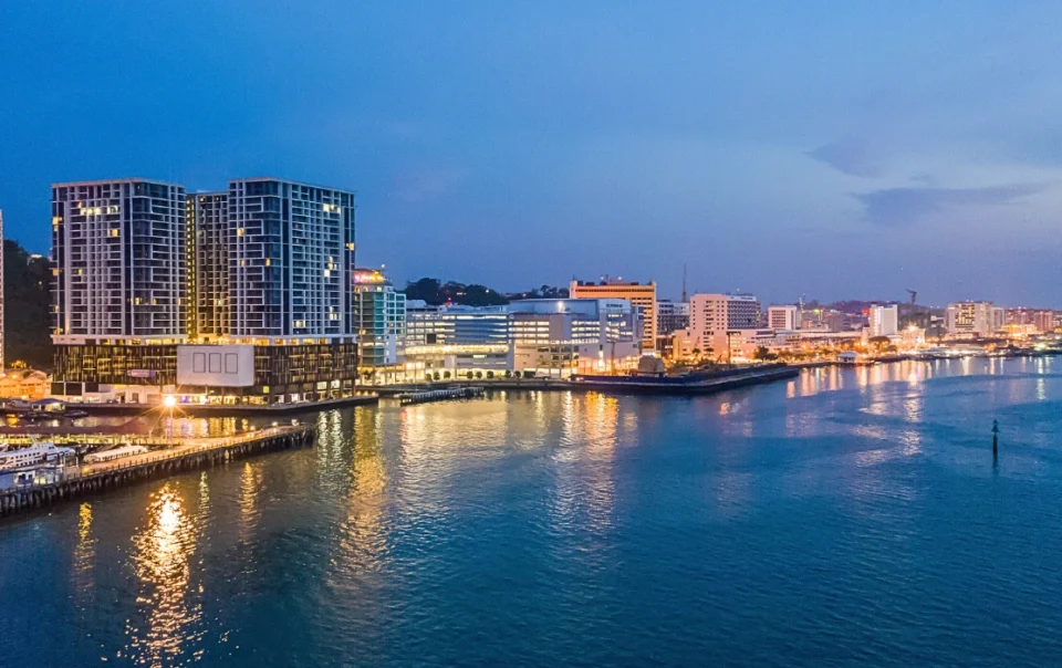 Night view of KK Waterfront with illuminated promenade, reflections on the water, and city lights- feature image for the blog: Filipino Market and KK Waterfront