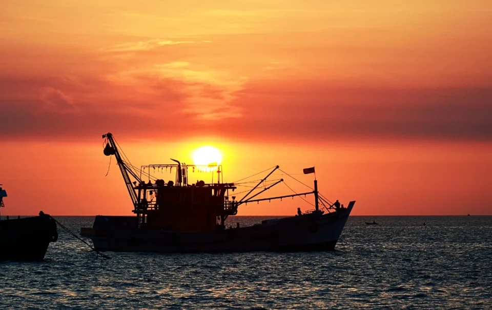 Orange sunset over the KK Waterfront with the silhouette of a boat on the calm sea in Kota Kinabalu
